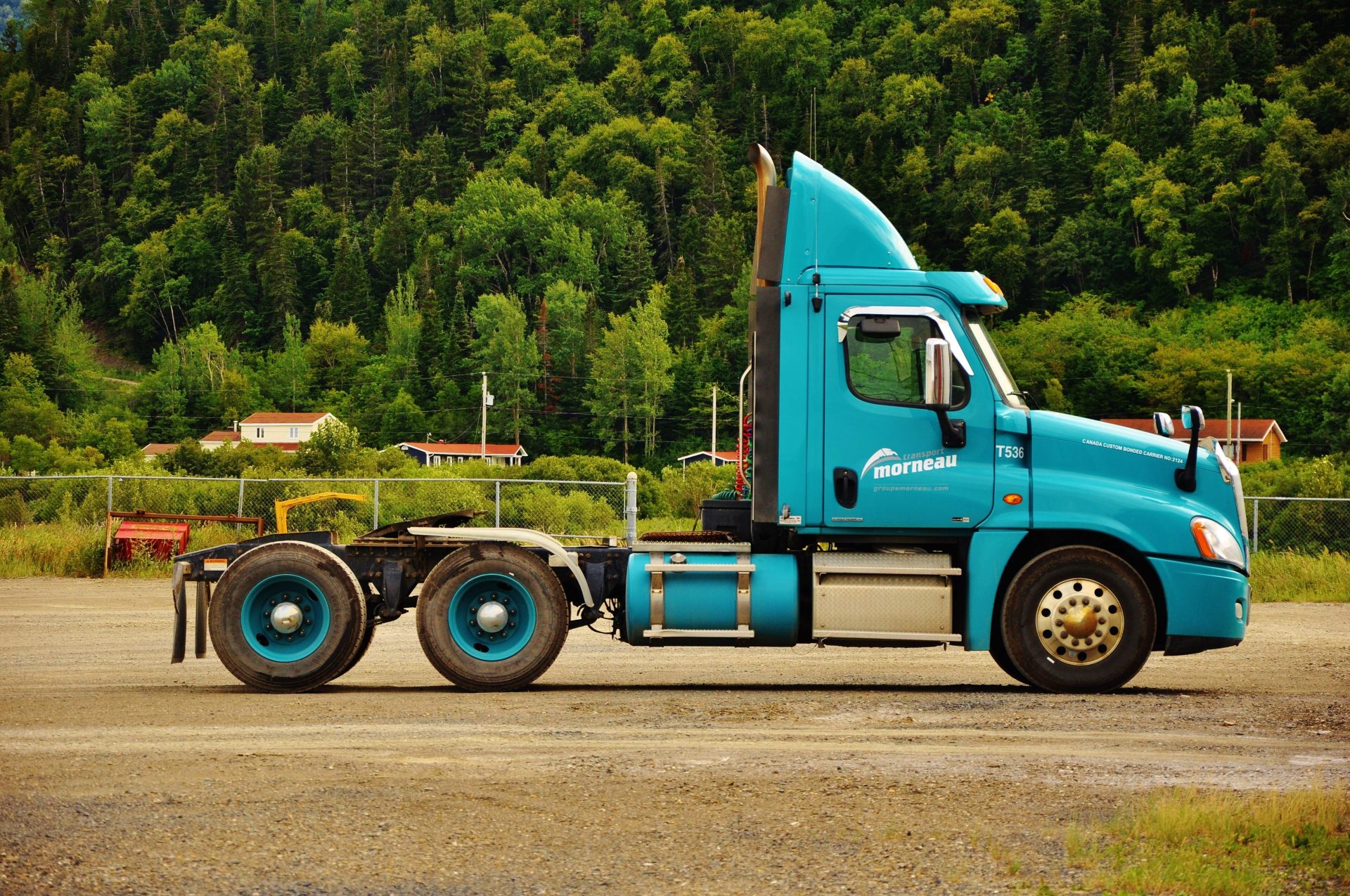 A blue truck parked on a dirt road against a forested backdrop in a rural area.